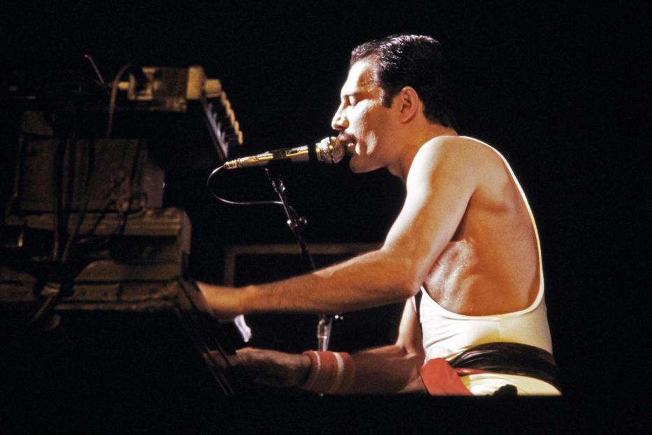 Freddie Mercury von Queen spielt Klavier und singt in ein Mikrofon.