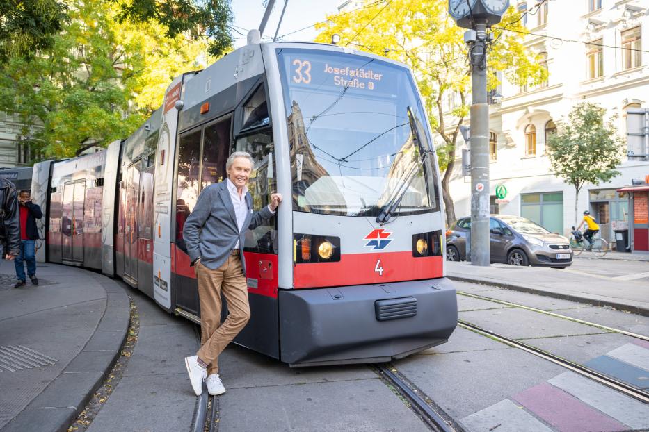 Ein Mann posiert vor einer Straßenbahn der Linie 33 in der Josefstädter Straße, Wien.
