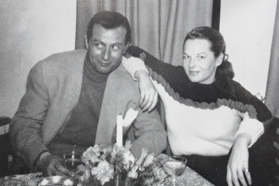 Ein Mann und eine Frau sitzen an einem Tisch mit Blumen und Getränken.