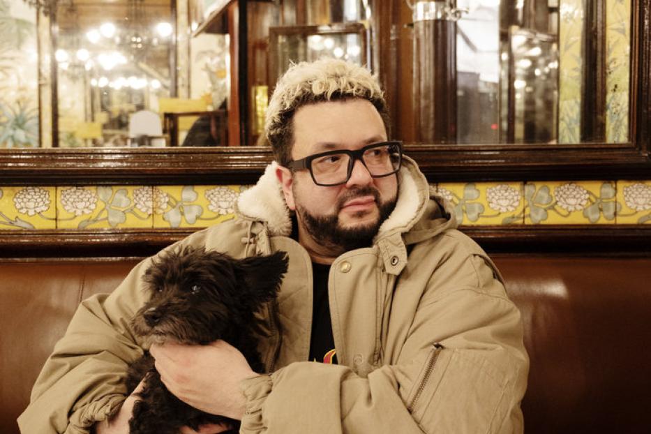 Ein Mann mit Brille hält einen kleinen schwarzen Hund in einem Restaurant.