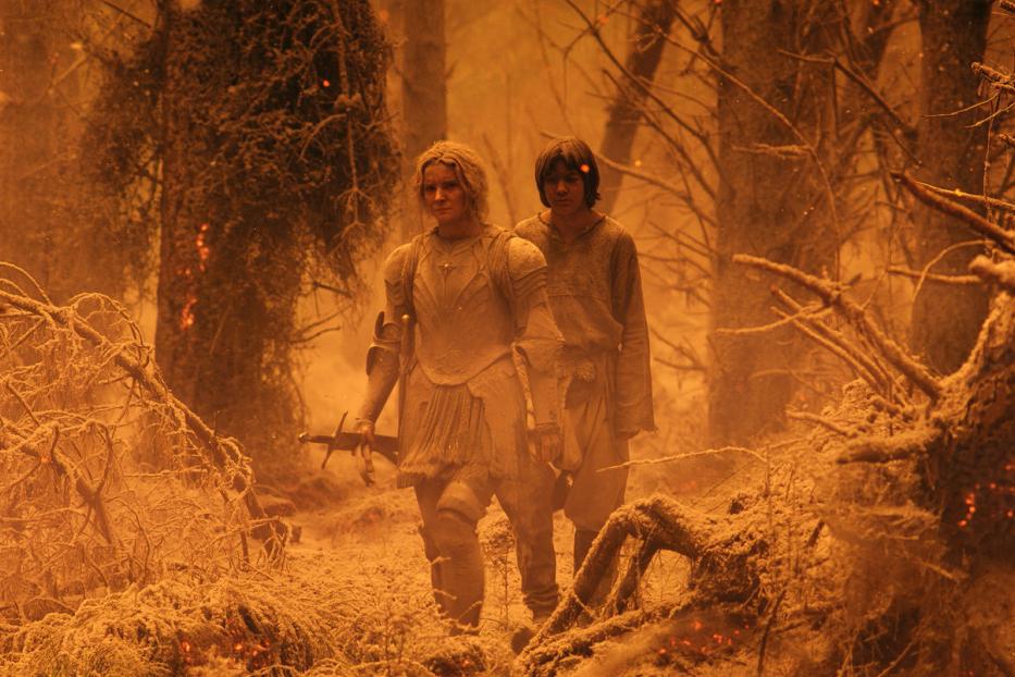 Galadriel und ein junger Mann stehen in einer zerstörten Waldlandschaft.