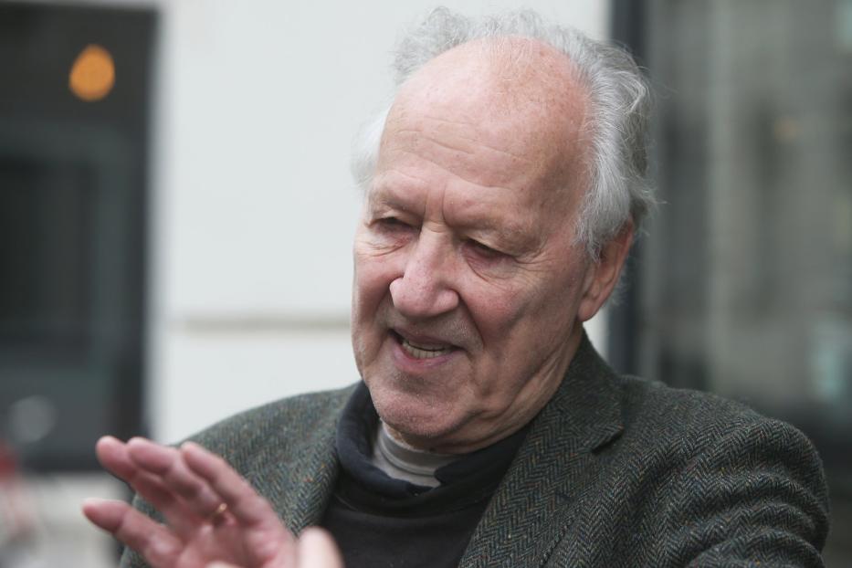 Ein älterer Mann mit grauem Haar gestikuliert mit der Hand.