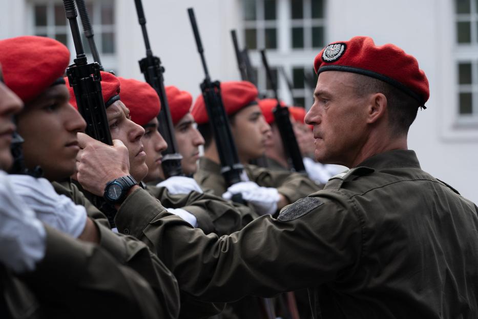 Eine Reihe von Soldaten in Uniform und roten Baretts steht mit Gewehren in Reih und Glied.