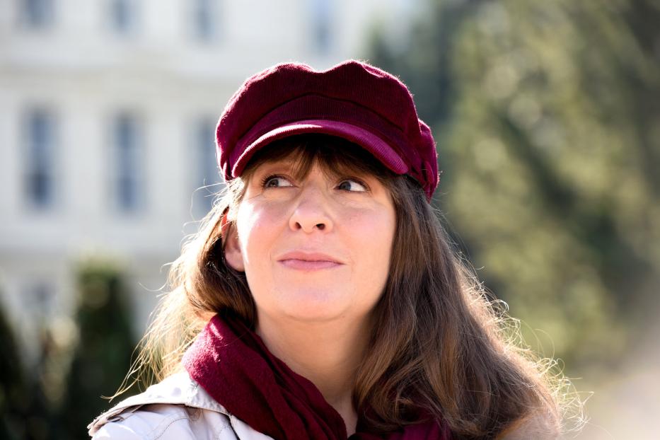 Eine Frau mit braunen Haaren, einem roten Hut und einem passenden Schal blickt nach oben.