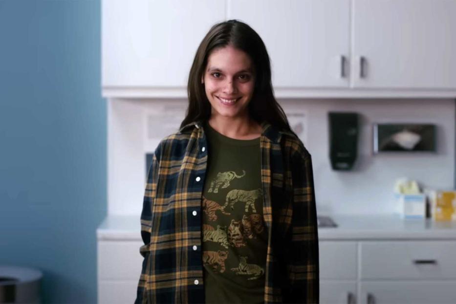 Eine lächelnde junge Frau mit einem T-Shirt mit Tigermotiv steht in einem Raum mit Schränken.