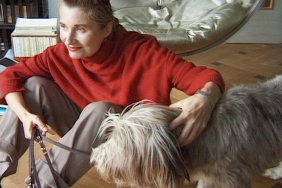 Eine Frau sitzt auf dem Boden und streichelt ihren zotteligen Hund.