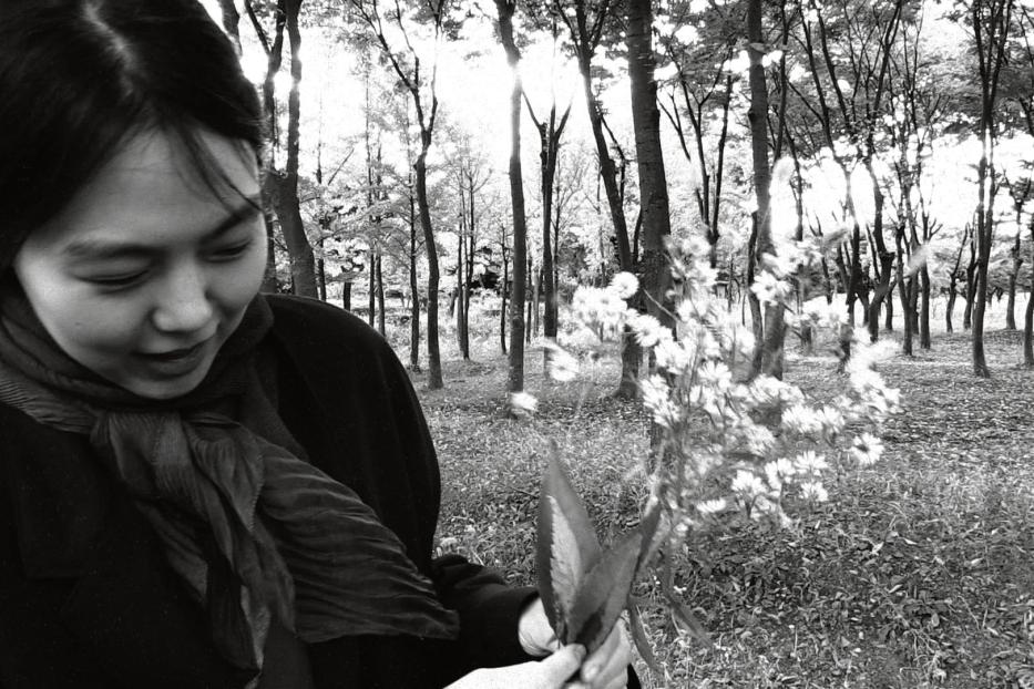 Eine Frau betrachtet einen Strauß weißer Blumen in einem Wald.