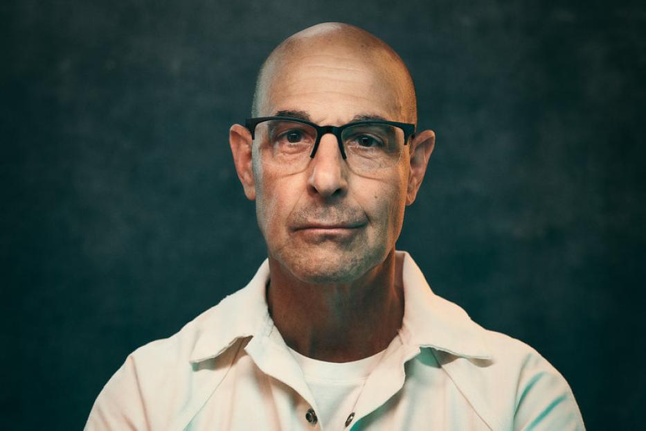 Stanley Tucci in einer hellen Uniform mit verschränkten Armen.