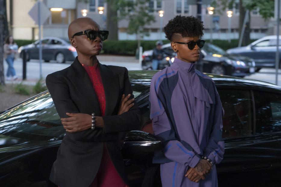 Okoye und Shuri, zwei Charaktere aus dem Film „Black Panther: Wakanda Forever“, posieren vor einem Auto.