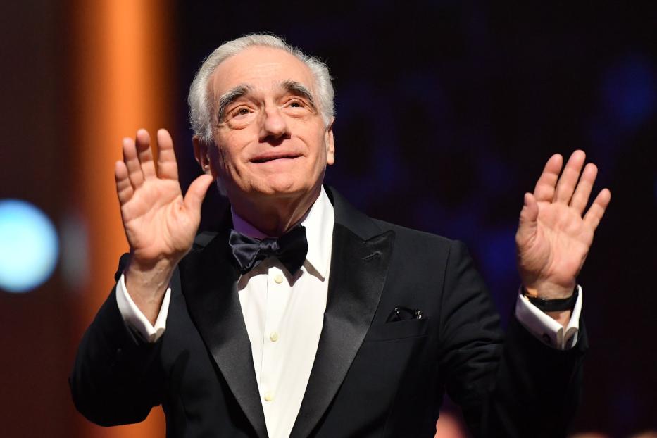 Martin Scorsese in einem Smoking mit Fliege hebt die Hände.