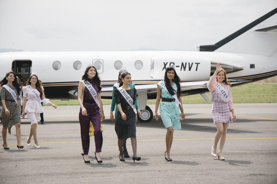 Mehrere Schönheitsköniginnen mit Schärpen und Diademen gehen vor einem Privatjet entlang.
