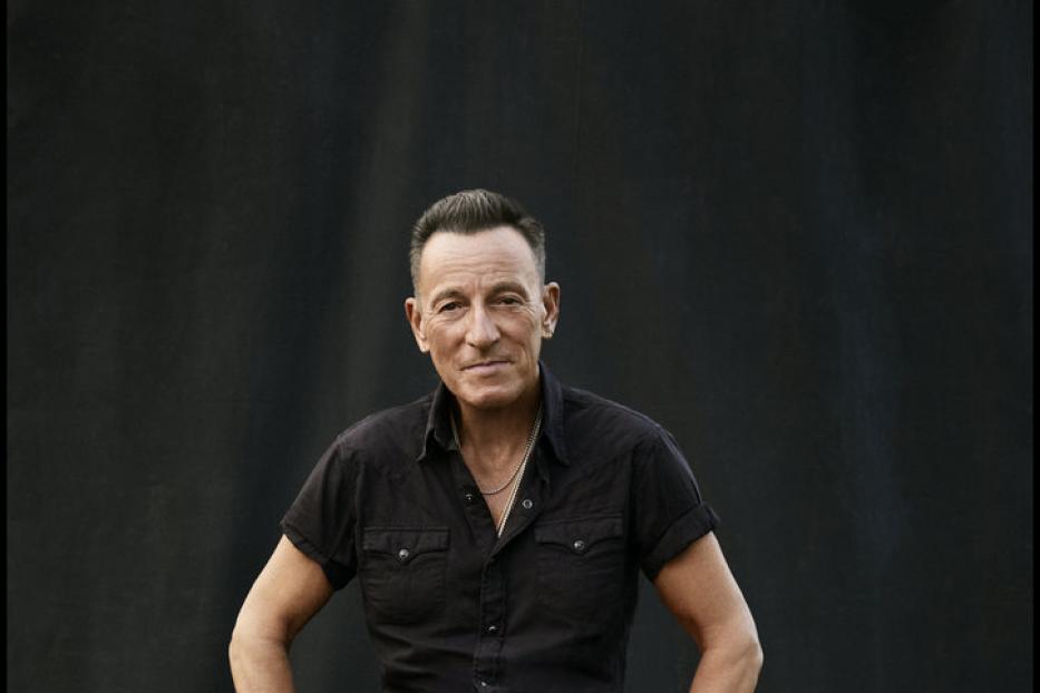 Bruce Springsteen sitzt auf einem Hocker vor einem schwarzen Hintergrund.