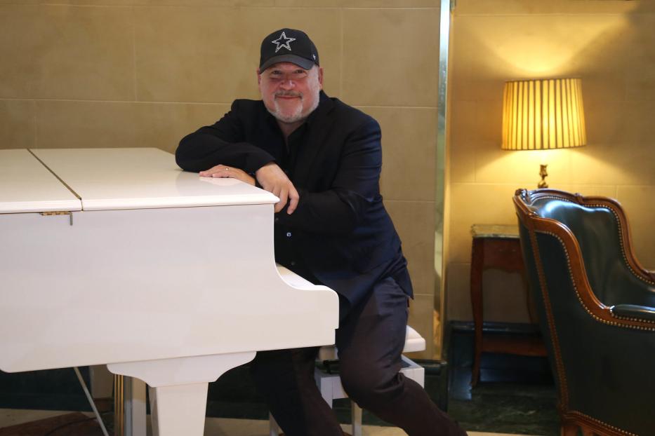 Ein Mann mit einer Dallas Cowboys-Kappe lehnt an einem weißen Klavier.