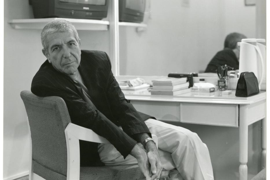 Leonard Cohen sitzt in einem Sessel vor einem Schminktisch mit Spiegel.