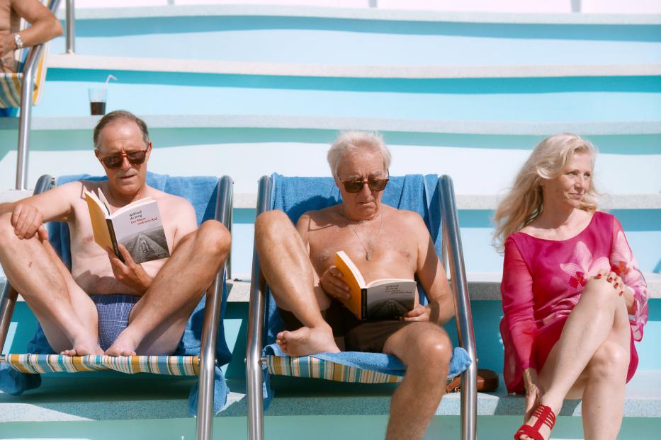 Drei ältere Personen entspannen am Pool und lesen das Buch „Wilfried de Jong – Ein Mann und sein Rad“.