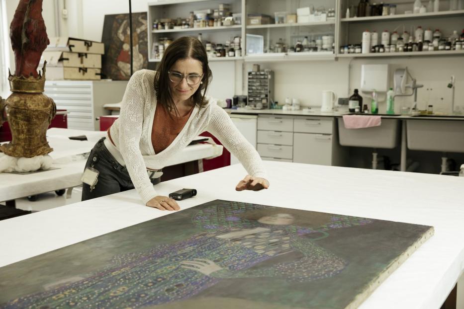 Eine Restauratorin untersucht ein Gemälde von Gustav Klimt auf einem Tisch.