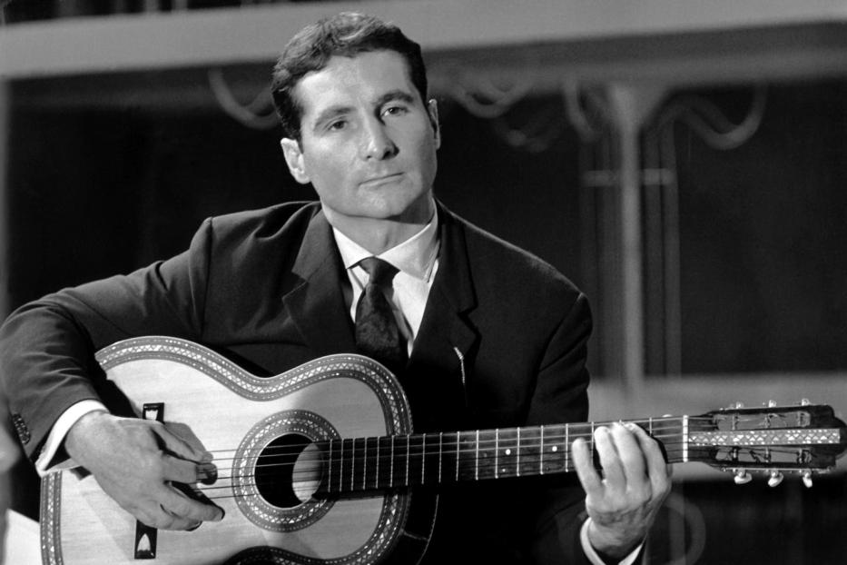 Ein Mann im Anzug spielt auf einer verzierten Gitarre.