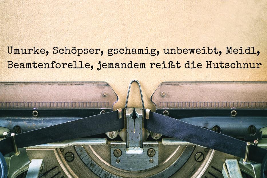 Eine Schreibmaschine mit dem Text „Umurke, Schöpser, gschamig, unbeweibt, Meidl, Beamtenforelle, jemandem reißt die Hutschnur“.