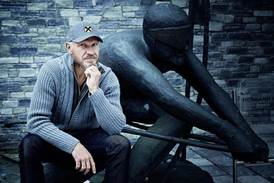 Ein Mann sitzt neben einer Statue des österreichischen Schwimmers Hermann Maier.