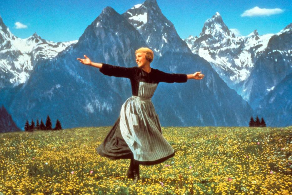 Julie Andrews als Maria tanzt auf einer Blumenwiese vor einer Bergkulisse im Film „The Sound of Music“.