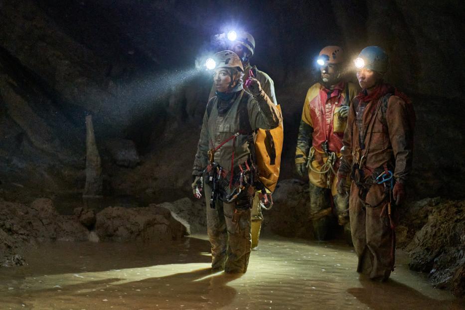 Eine Gruppe von Höhlenforschern watet durch das Wasser in einer dunklen Höhle.