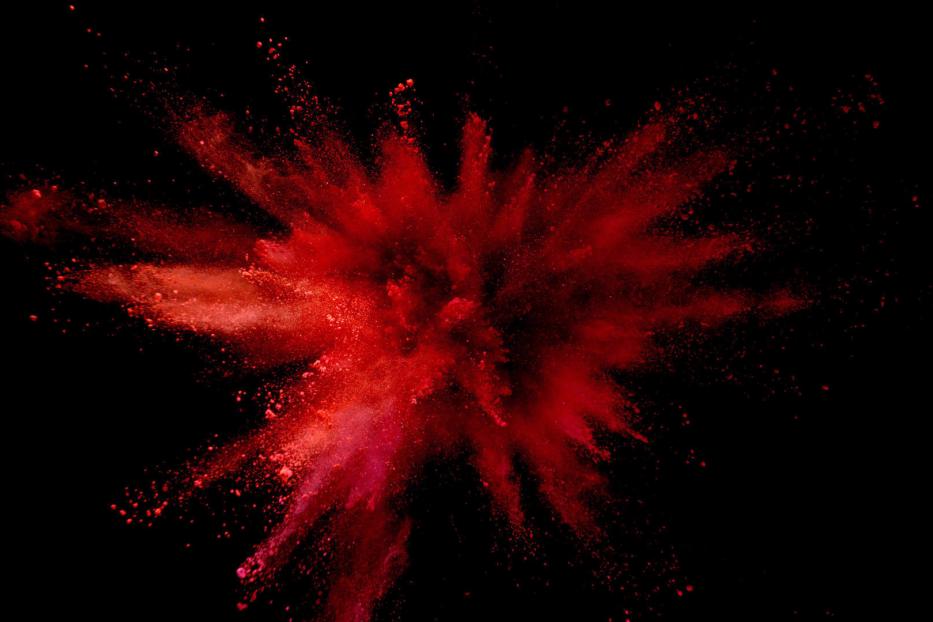 Eine rote Farbpulverexplosion vor einem schwarzen Hintergrund.