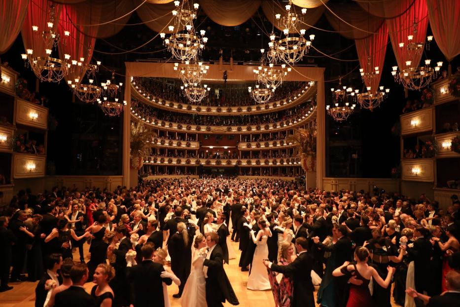 Ein großer Ballsaal mit vielen Paaren beim Tanzen unter funkelnden Kronleuchtern.