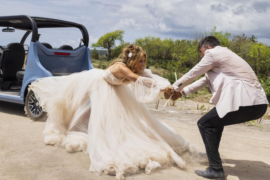 Eine Braut im Hochzeitskleid wird von einem Mann auf einem staubigen Feld zurückgehalten.