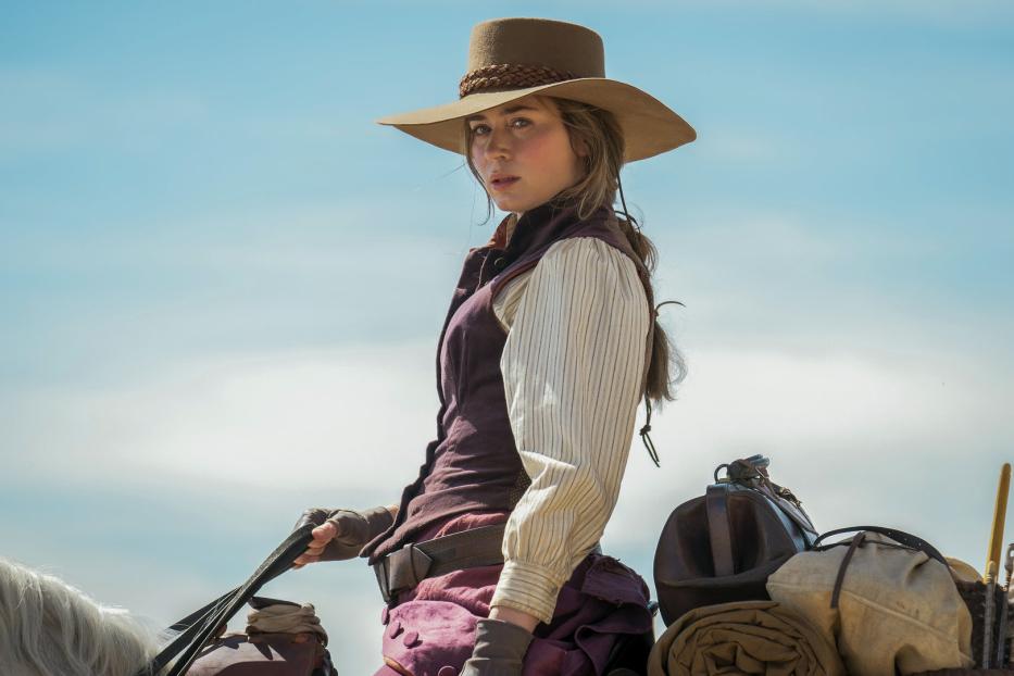 Emily Blunt reitet in Westernkleidung auf einem Pferd vor blauem Himmel.