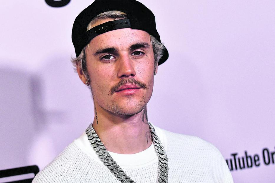 Justin Bieber mit Kappe und auffälliger Halskette vor einem lila Hintergrund.