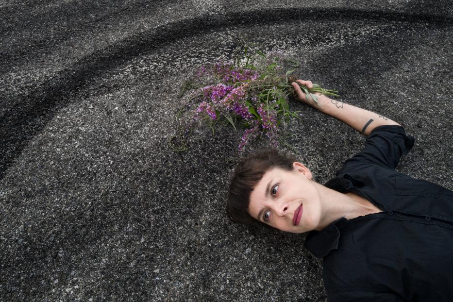Eine Frau liegt auf dem Asphalt und hält einen Strauß lila Blumen.