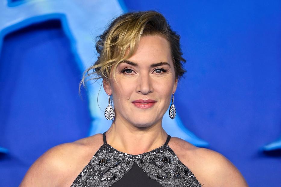 Ein Porträt von Kate Winslet mit silbernen Ohrringen vor einem blauen Hintergrund.