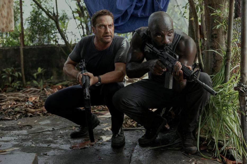 Gerard Butler und Idris Elba zielen mit Gewehren in einer Dschungelartigen Umgebung.