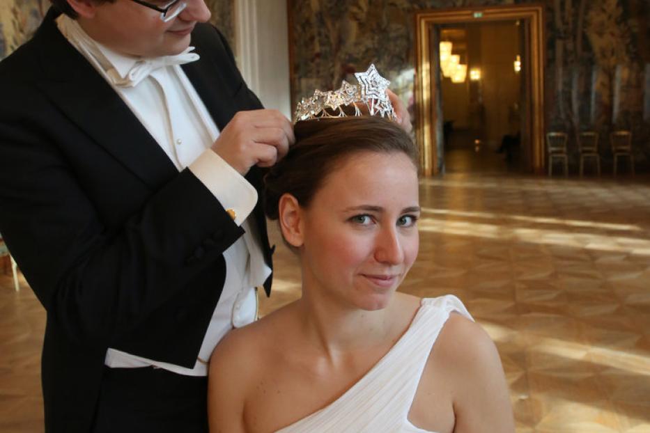 Ein Mann im Smoking setzt einer Frau im weißen Kleid eine Tiara auf.
