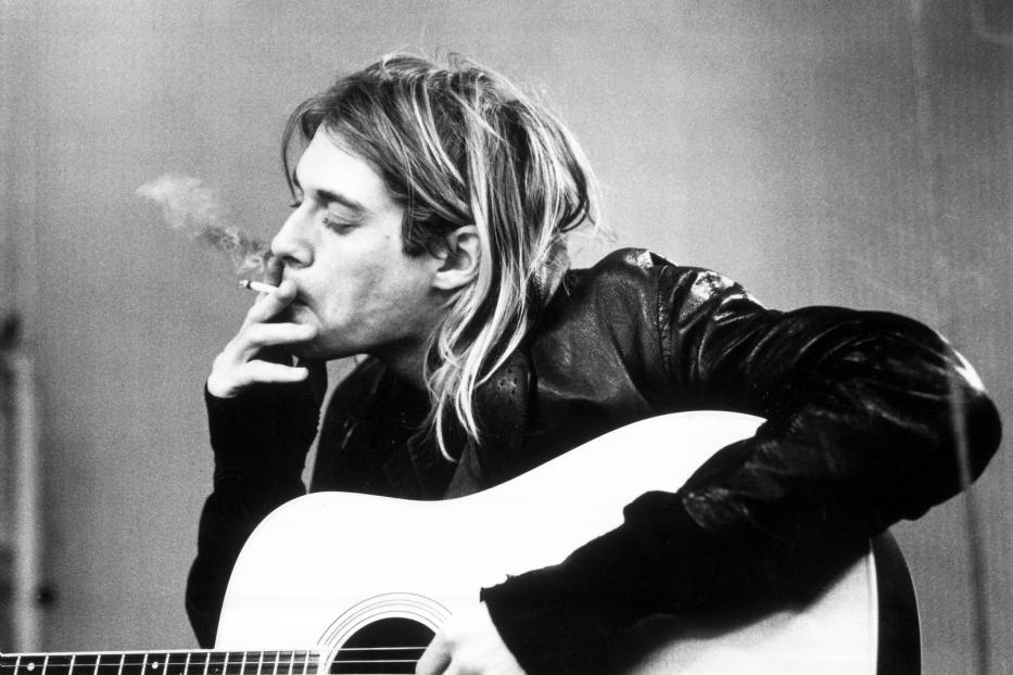 Kurt Cobain mit Gitarre und Zigarette in Schwarzweiß.