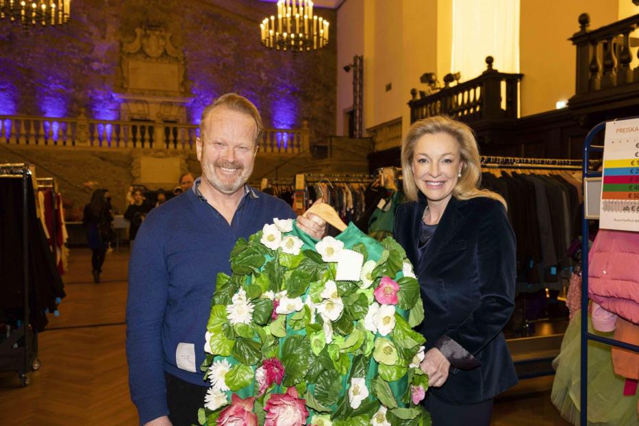 Zwei Personen halten eine Jacke, die mit Blumen und Blättern verziert ist.