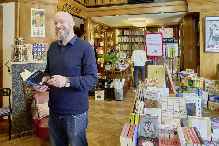 Ein Mann mit Buch steht in einem Buchladen mit japanischer Literatur.