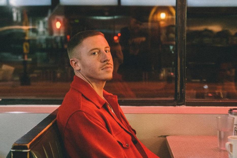 Macklemore sitzt in einem roten Anzug in einem Diner.
