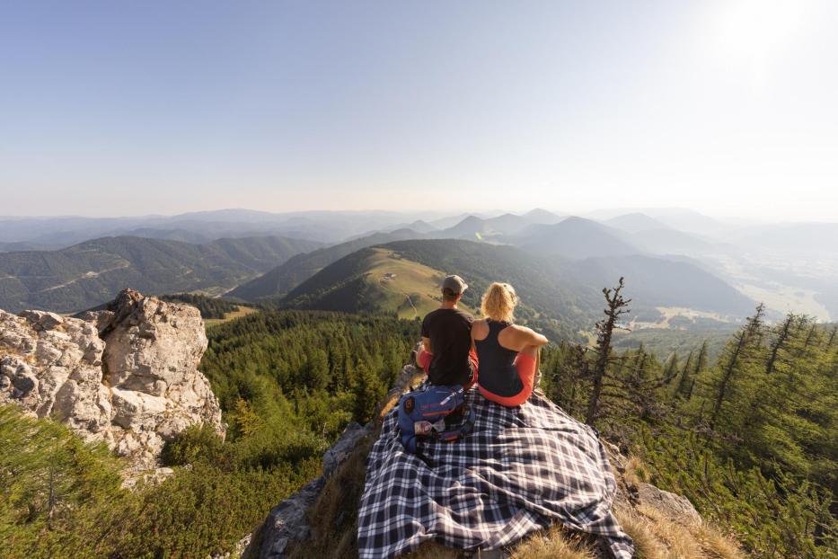 Ein Paar sitzt auf einer Decke auf einem Berggipfel und blickt in die Ferne.
