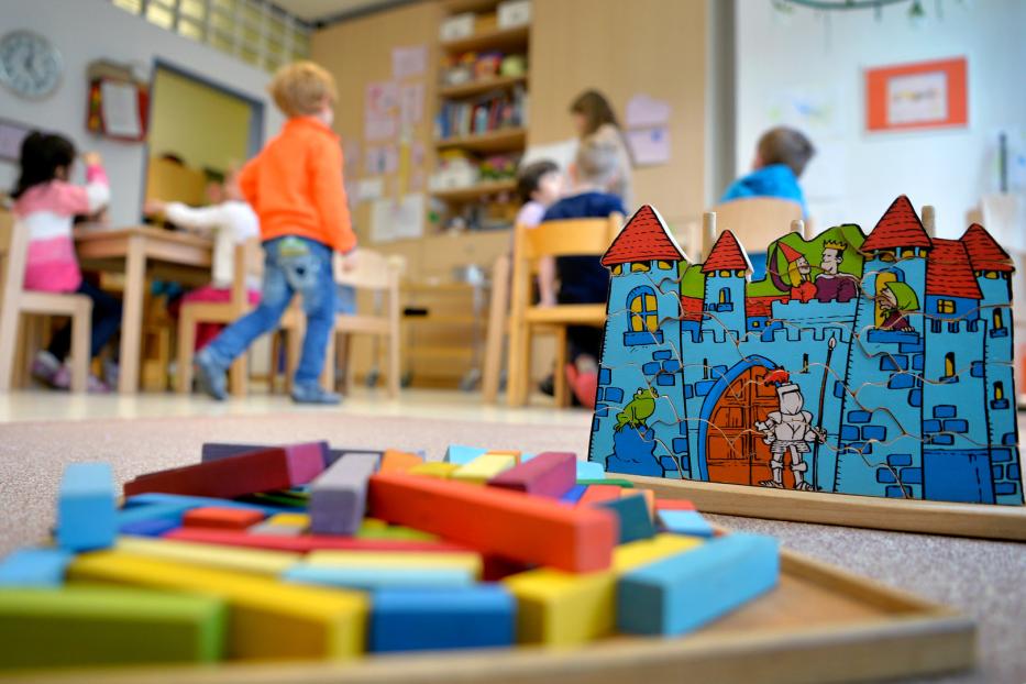 Kinder spielen mit einem Holzpuzzle und Bausteinen in einem Kindergarten.