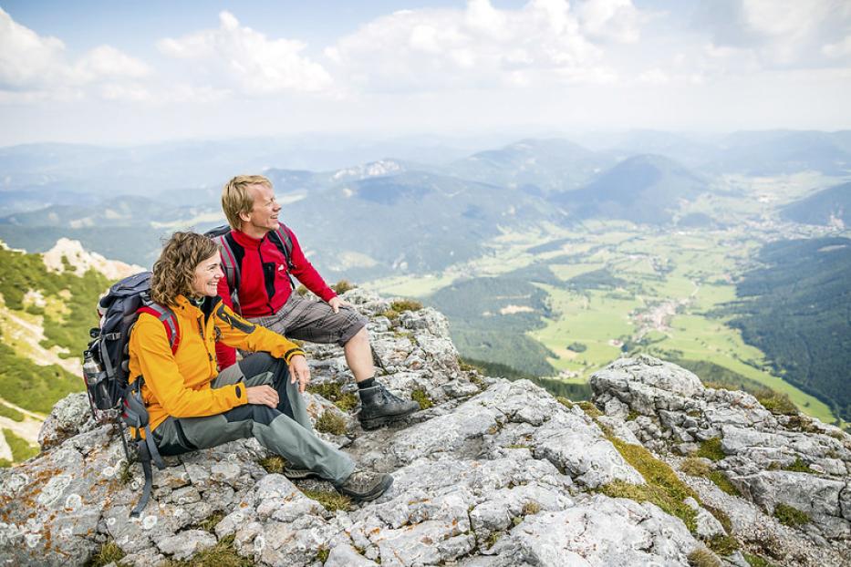Eine Frau und ein Mann sitzen auf einem Felsen und genießen die Aussicht auf einem Berg.