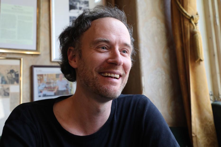 Ein lächelnder Mann mit Bart sitzt in einem Café.
