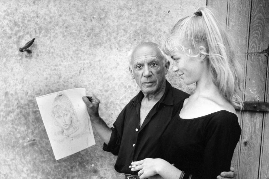 Pablo Picasso mit einer jungen Frau und einer Porträtzeichnung in der Hand.