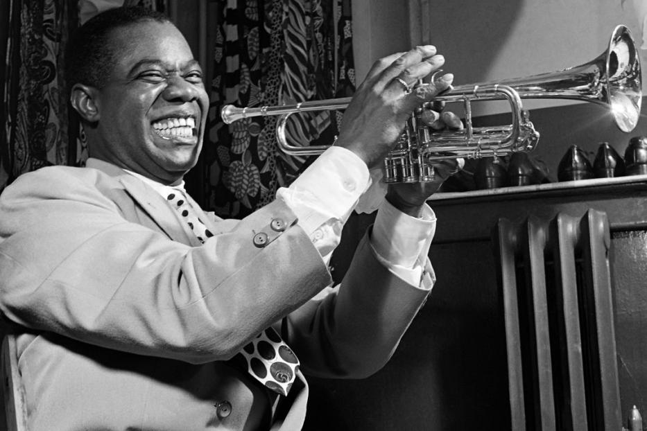 Louis Armstrong spielt Trompete und lächelt.