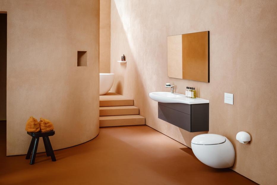 Ein Badezimmer in Erdtönen mit Waschbecken, Toilette und Badewanne auf einem Podest.