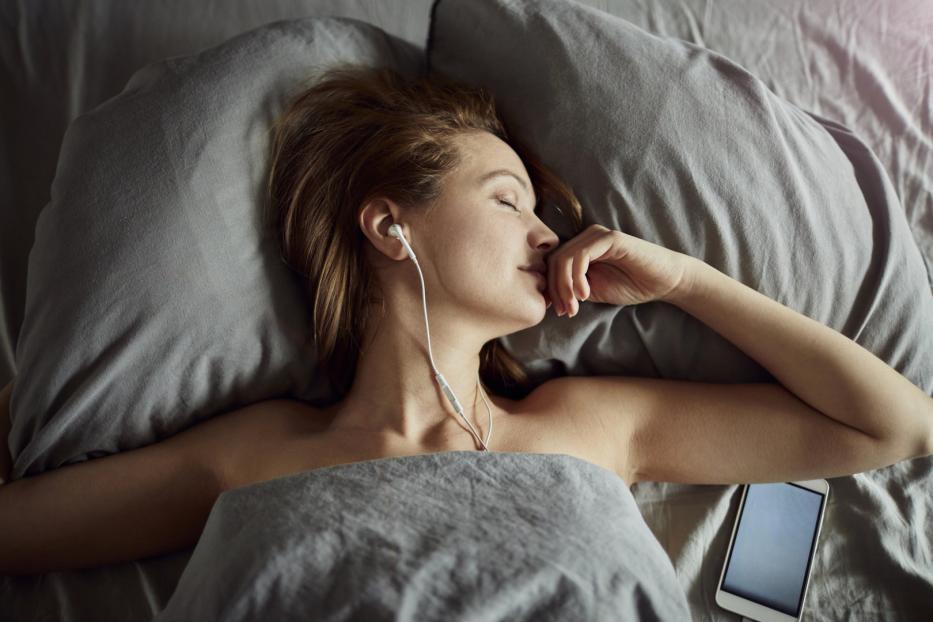 Eine Frau liegt mit Kopfhörern im Bett und schläft.