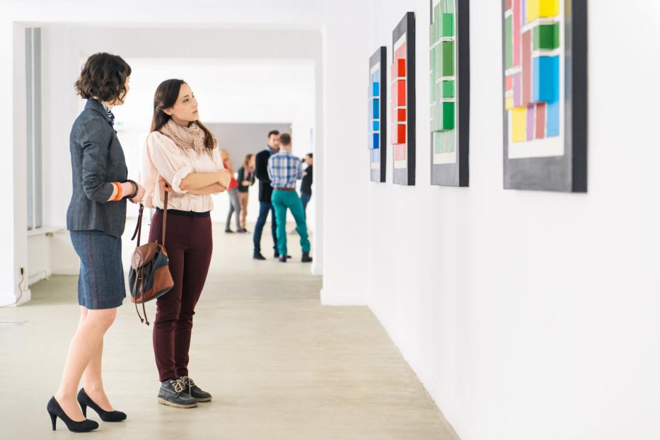 Zwei Frauen betrachten farbenfrohe, abstrakte Kunstwerke in einer Galerie.
