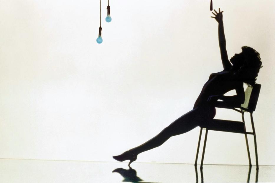 Die Silhouette einer Frau, die auf einem Stuhl sitzt und nach einem Lichtschalter greift, erinnert an „Flashdance“.