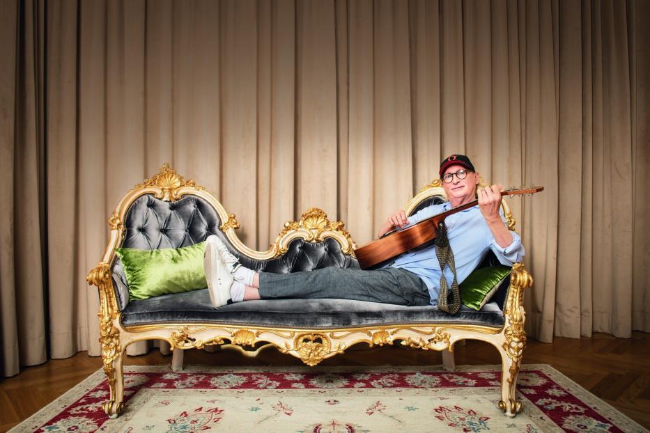 Ein Mann liegt auf einem verzierten Sofa und spielt Gitarre.