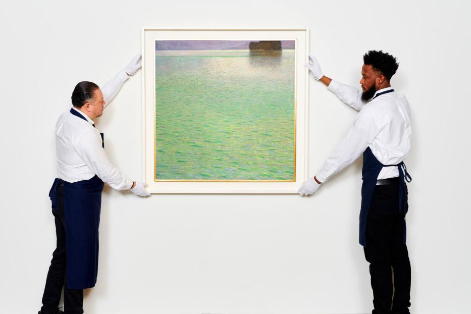 Zwei Personen in Arbeitskleidung hängen ein Landschaftsgemälde an eine weiße Wand.
